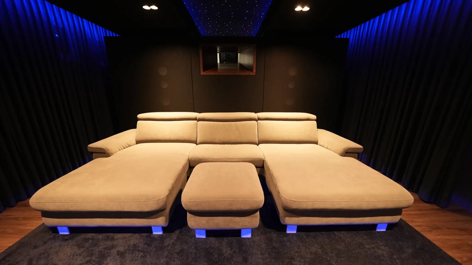 Heimkino mit niedriger Leinwand, umlaufender Couch, blauer Lichtvoute und Sternenhimmel im Deckensegel.