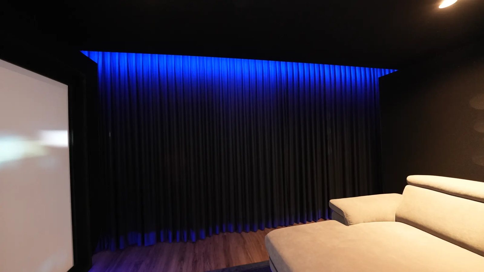 Dunkle Vorhangwand mit blauer Lichtvoute im Heimkino, links der Rand der Leinwand.
