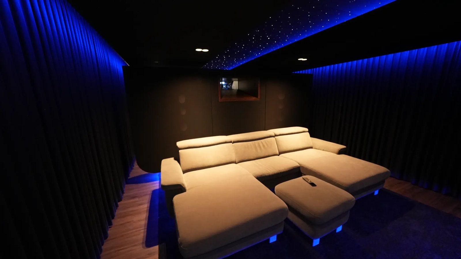 Motorisierte Couch mit Hocker und Fernbedienung, dahinter Sternenhimmel und Spiegel im Heimkino.